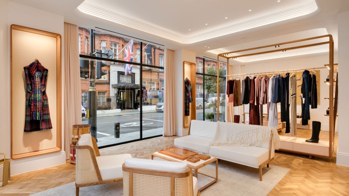 Upscale clothing boutique interior with elegant seating, stylish garments on display, and large street-facing windows.