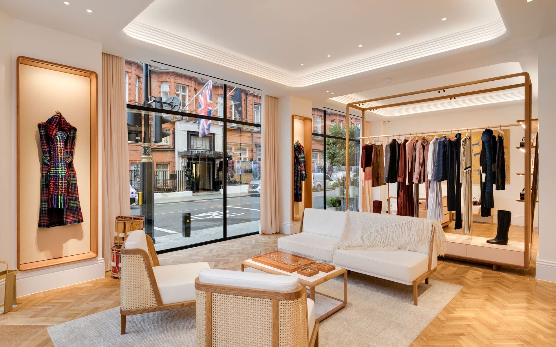 Upscale clothing boutique interior with elegant seating, stylish garments on display, and large street-facing windows.