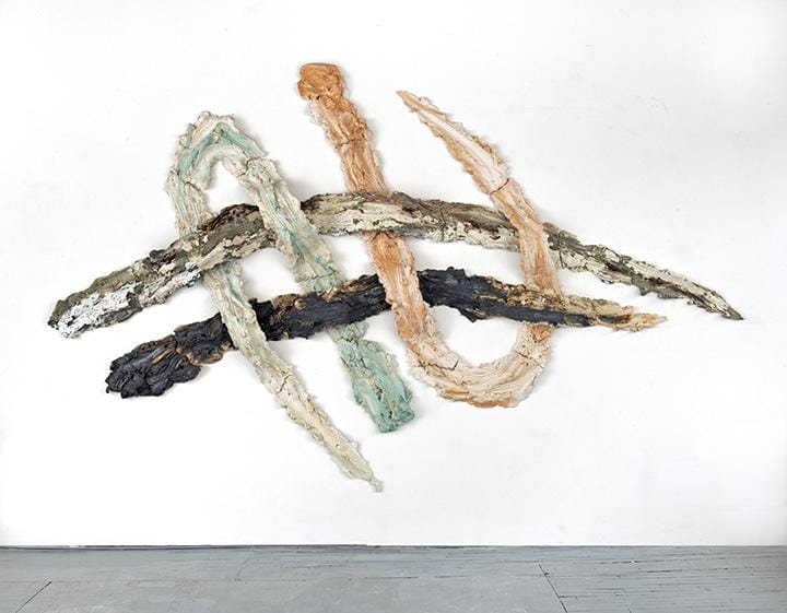 Abstract wall sculpture with intertwined textured elements in earth tones and muted colors on a plain white background.