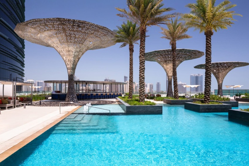 Luxurious outdoor pool with modern sunshades and palm trees, overlooking a city skyline in the background.