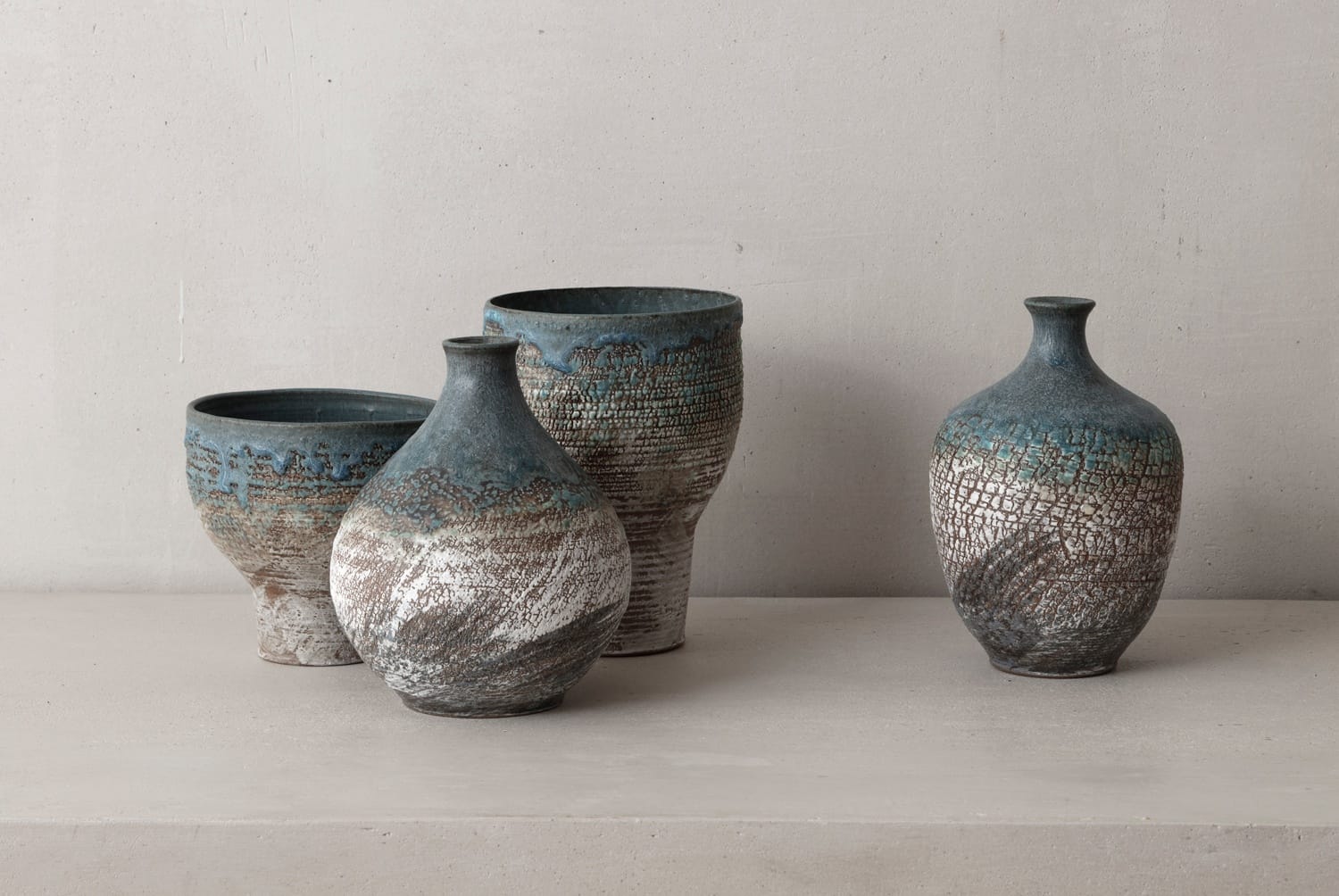 Four textured ceramic vases with blue and white designs placed on a plain surface against a light gray background.
