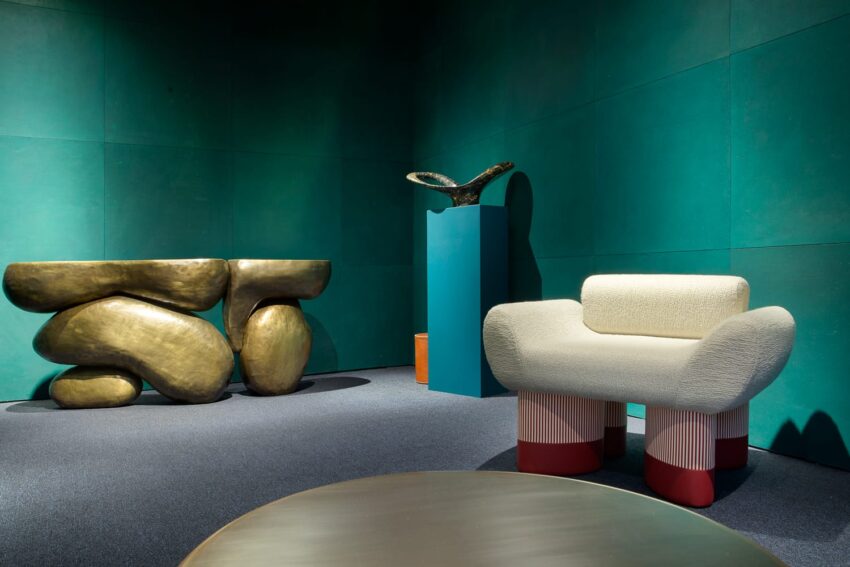 Modern art deco room with a curvy chair, abstract bronze console, teal wall, and sculpture on pedestal.