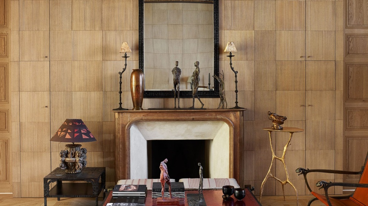 Elegant living room with fireplace, decorative statues on mantel, large mirror, and eclectic furniture in warm tones.