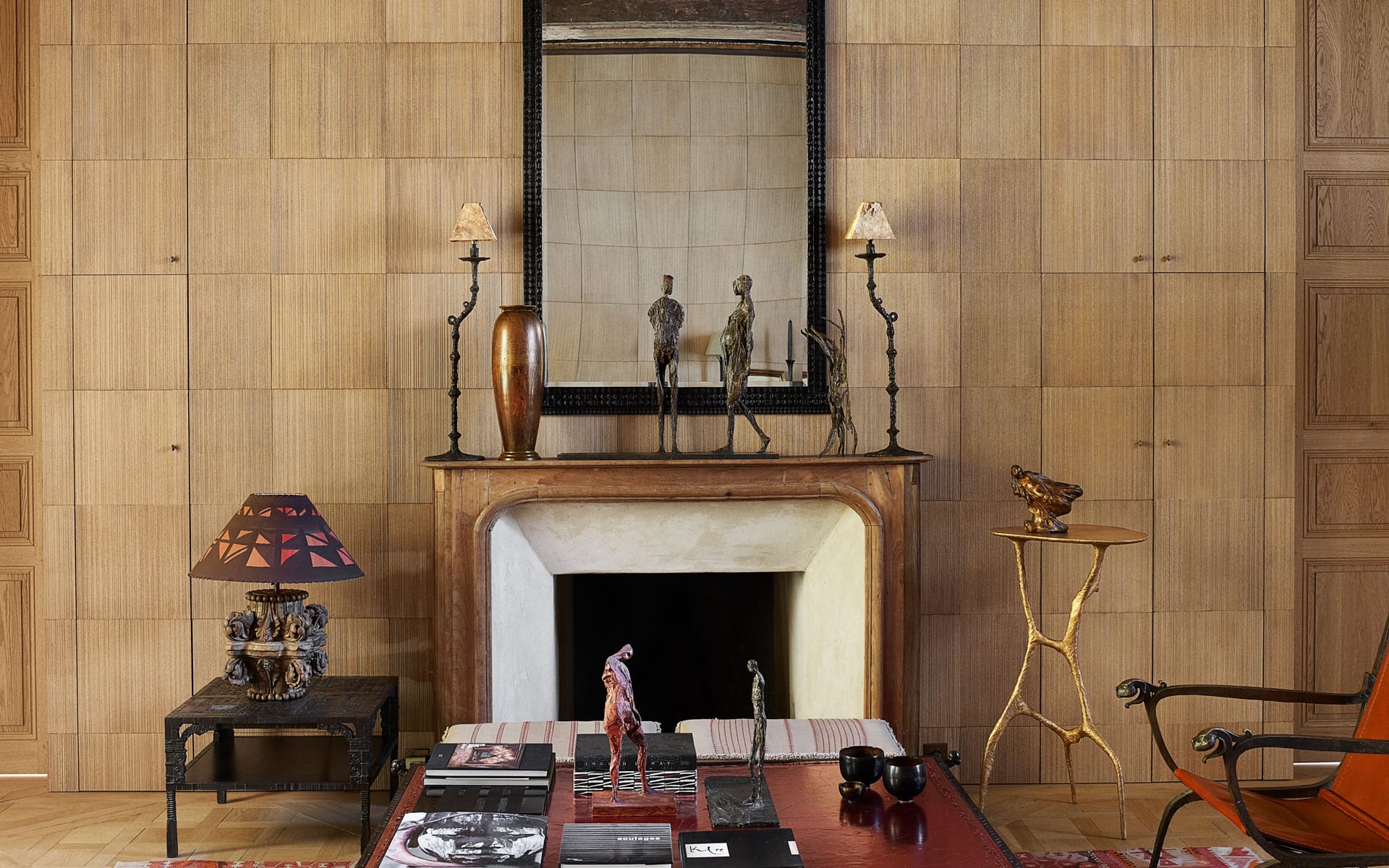 Elegant living room with fireplace, decorative statues on mantel, large mirror, and eclectic furniture in warm tones.