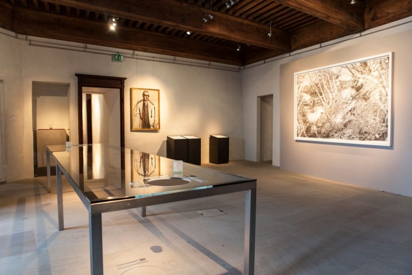 Modern art gallery interior with large framed black and white photos on walls, glass table, and soft overhead lighting.