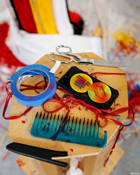 Artistic setup with scissors, blue tape, a comb, and a phone displaying colorful text, all on a wooden table.