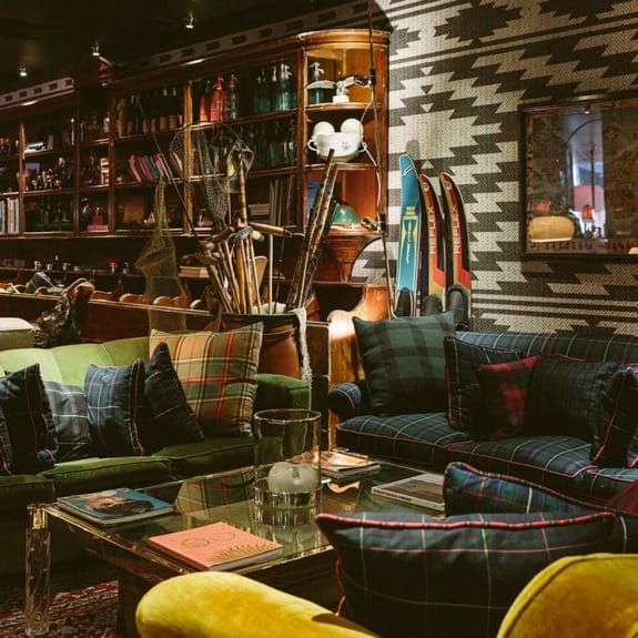 Cozy living room with plaid sofas, bookshelves, and vintage decor, including skis and fishing rods.