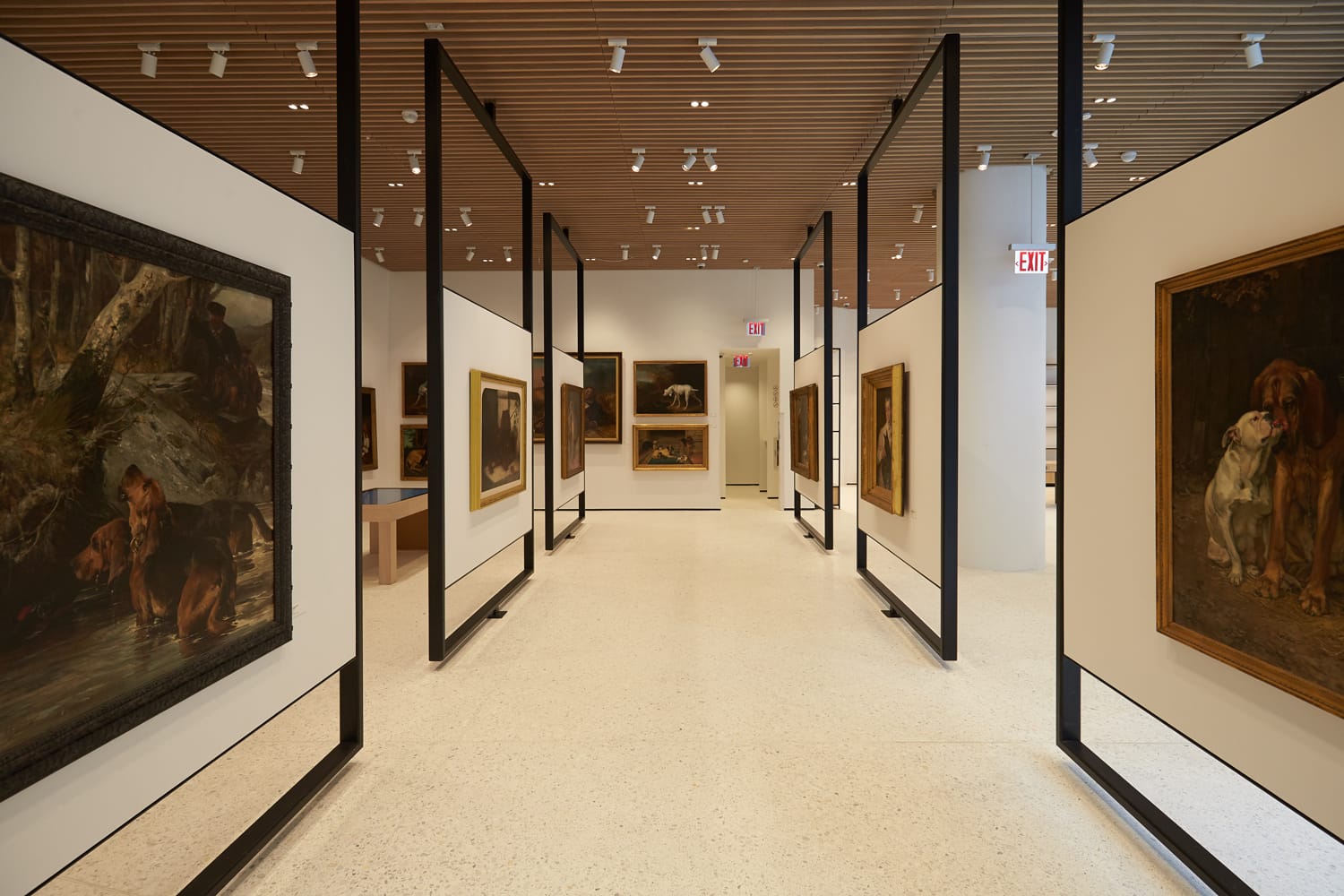 Art gallery interior with paintings of dogs on display on white walls, wooden ceiling, and overhead lights.