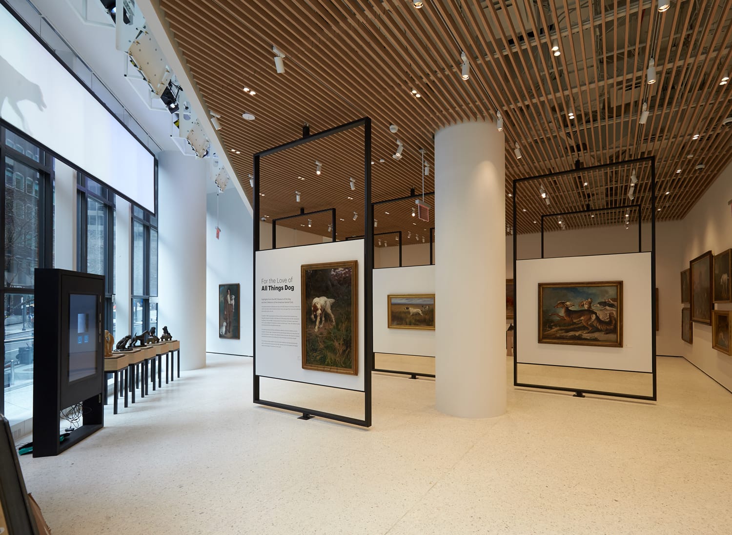 Modern art gallery interior with paintings on display and large windows letting in natural light.