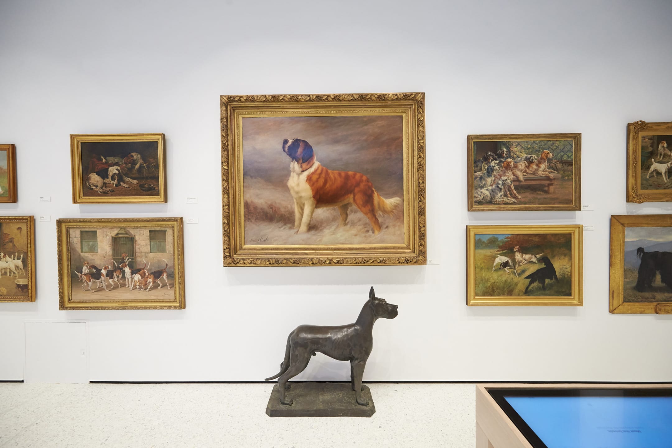 Art gallery wall featuring a large dog painting surrounded by various dog-themed artworks and a dog sculpture in front.
