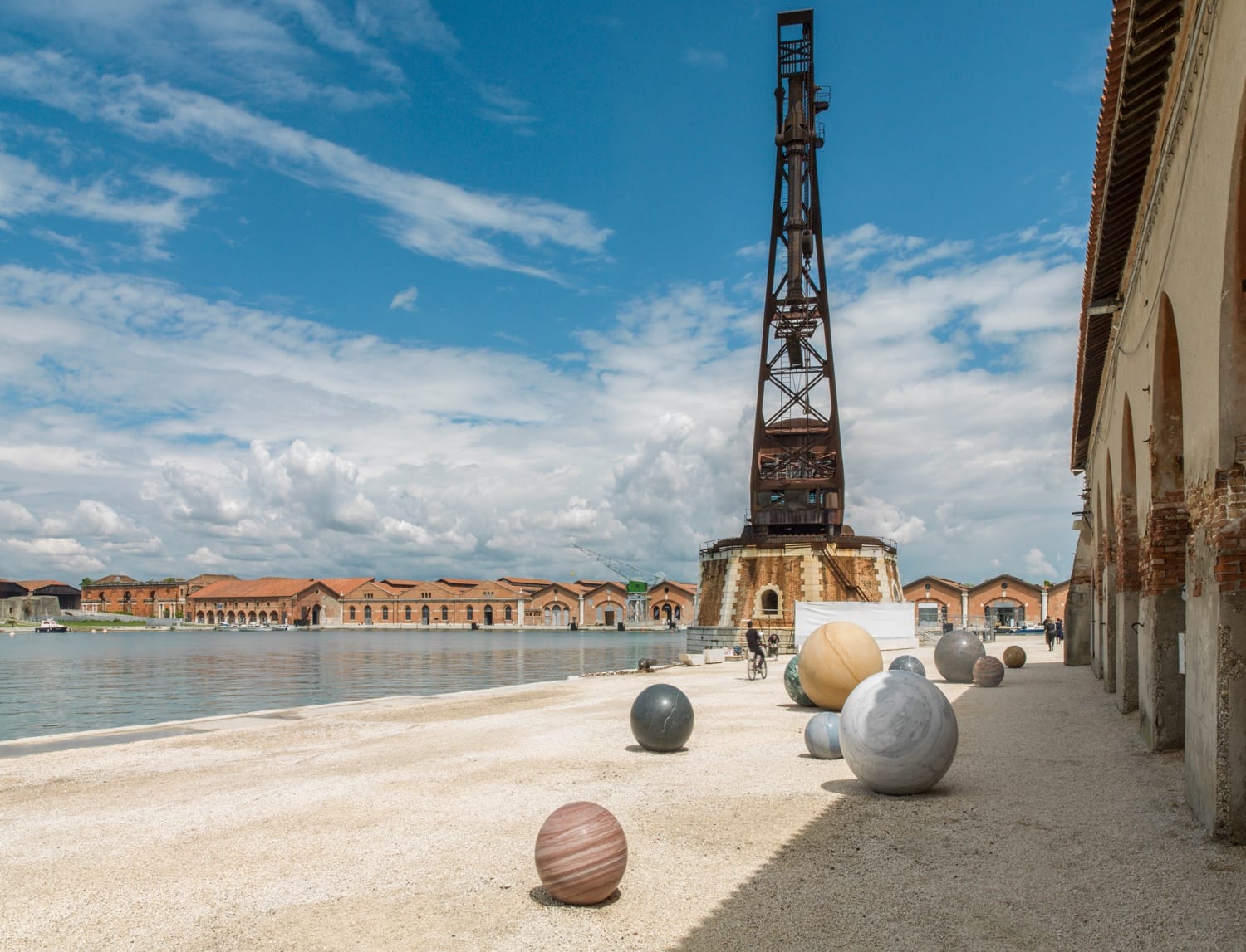 Art installation with spherical sculptures on a waterfront plaza, featuring a tall metal structure in the background.