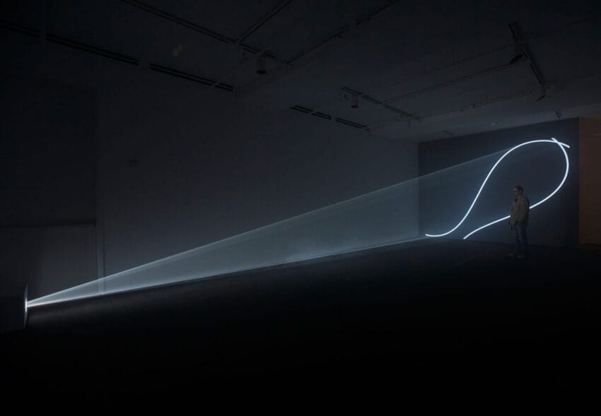 Art installation featuring a light projection forming a looping line on a wall in a dimly lit room with a person observing.
