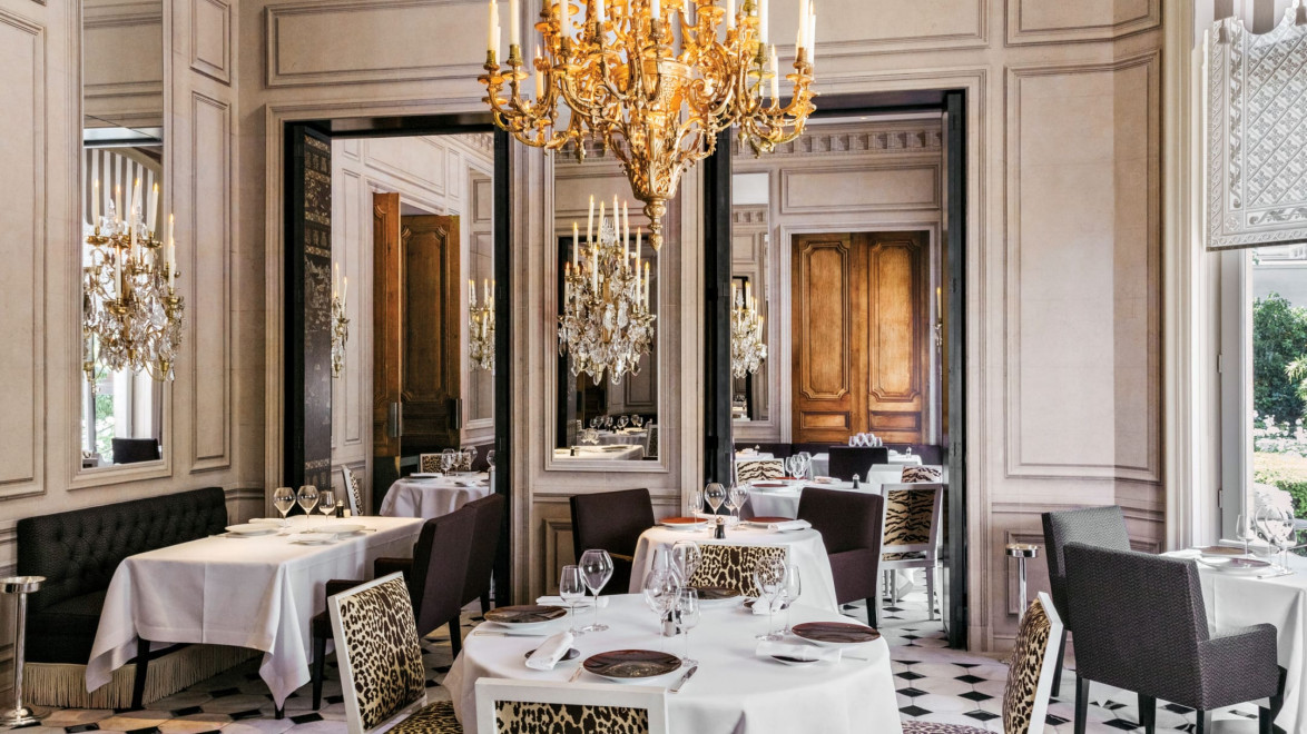 Elegant restaurant interior with chandeliers, white tablecloths, and decorative mirrors, featuring stylish animal print chairs.