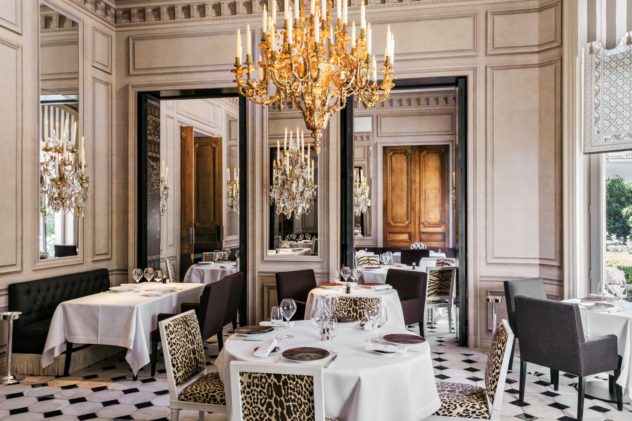 Elegant restaurant interior with chandeliers, white tablecloths, and decorative mirrors, featuring stylish animal print chairs.