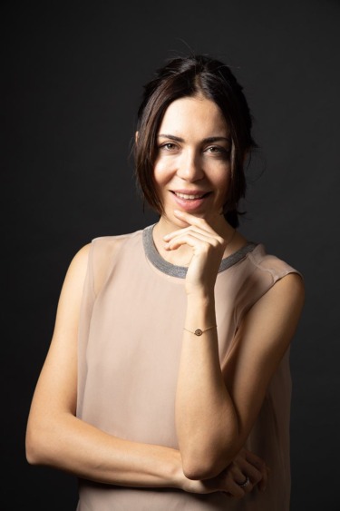 Woman posing confidently with hand on chin, wearing a sleeveless top against a dark background.