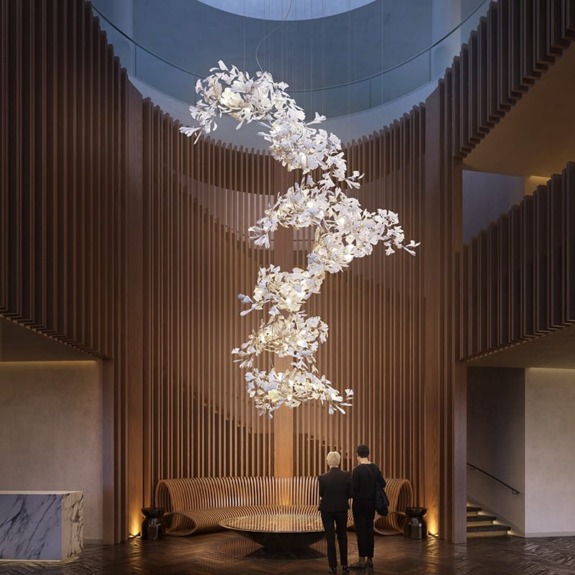 Two people admire a large, artistic chandelier made of delicate, white sculptural elements in a modern lobby.