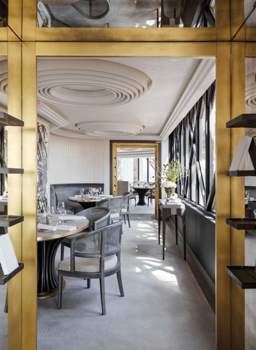 Elegant restaurant interior with gold accents, modern decor, round tables set for dining, and large windows letting in natural light.