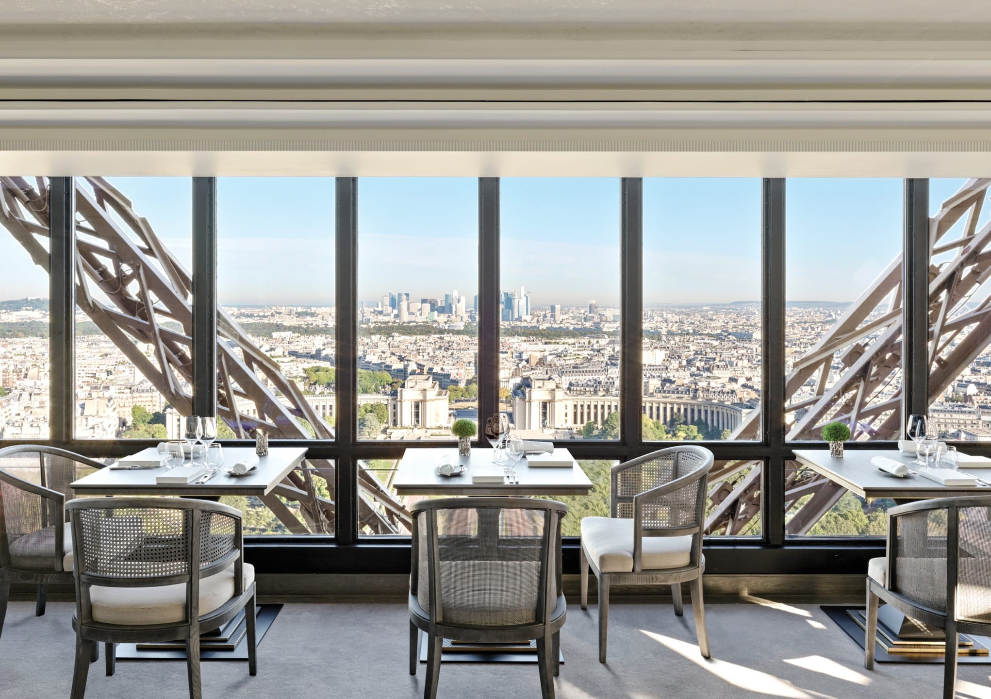 Dining area with tables and chairs offering a panoramic view of a cityscape through large windows in an elevated setting.