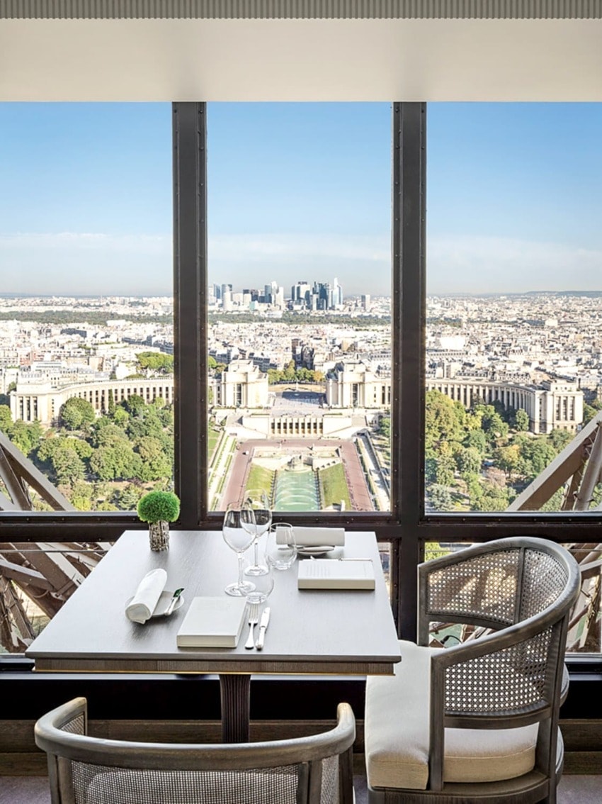 Elegant dining table with cityscape view through large window showcasing historical buildings and expansive skyline.
