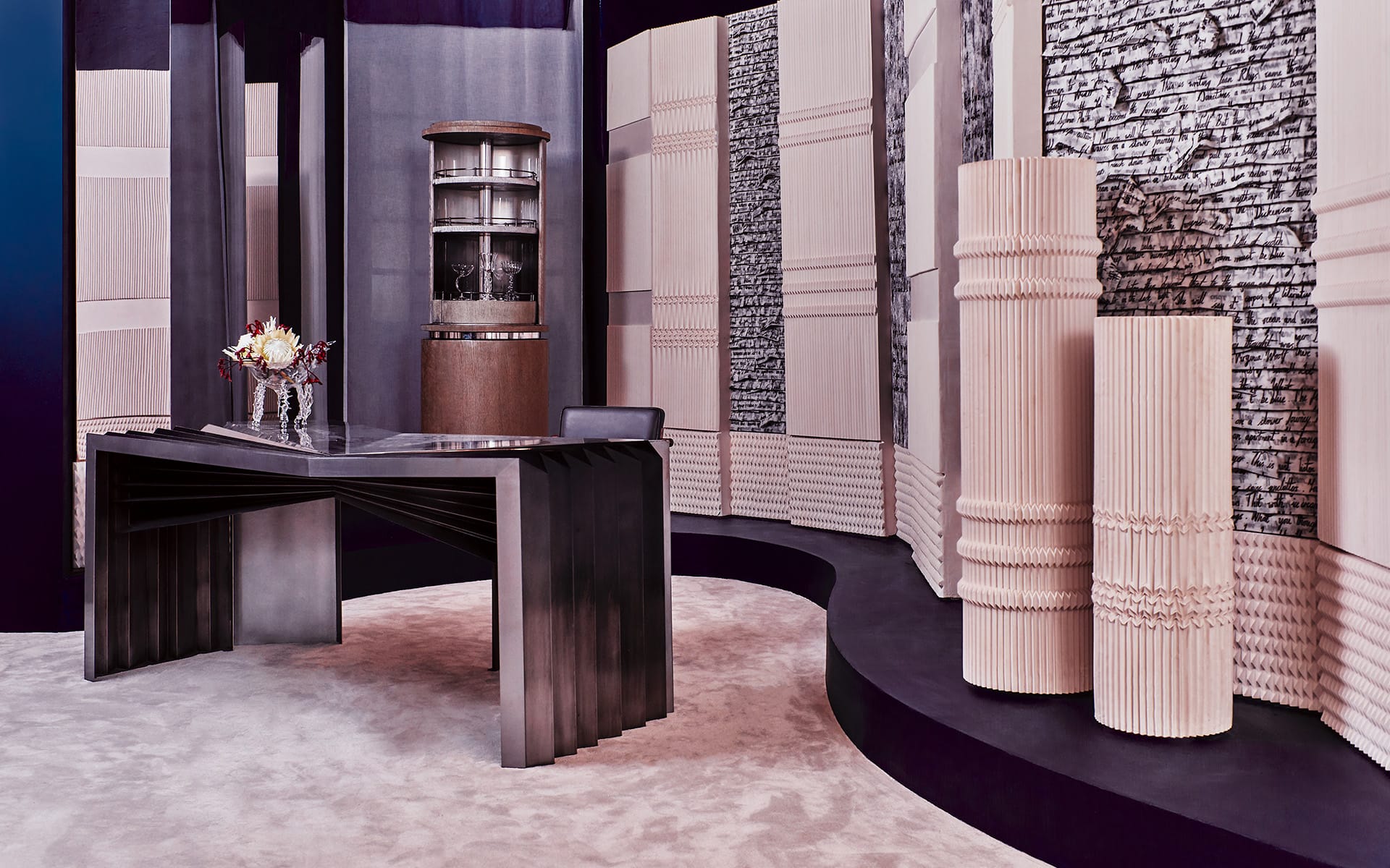 Modern interior with a sleek black desk, tall textured columns, a vase with flowers, and intricate wall designs.