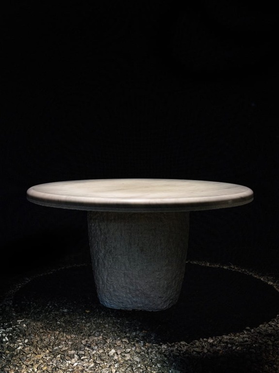 Round stone table on a gravel surface against a dark background.