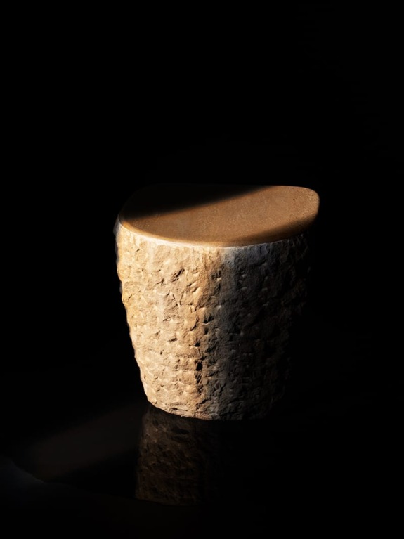 Smooth beige stone stool on dark background with light casting a shadow.