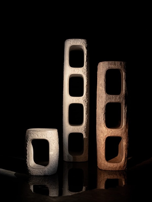 Three tall, rectangular stone sculptures with hollow interiors, illuminated against a dark background.