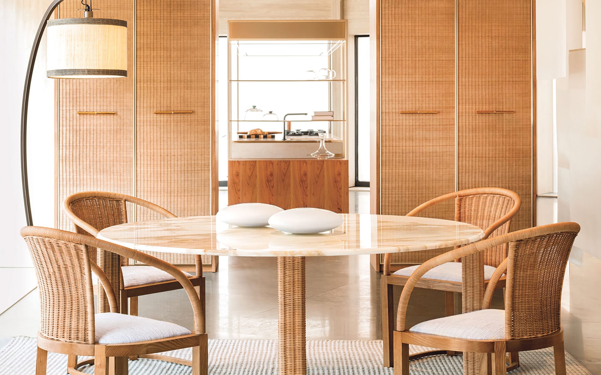 Round marble dining table with four wicker chairs in a modern room with wooden cabinets and a floor lamp.