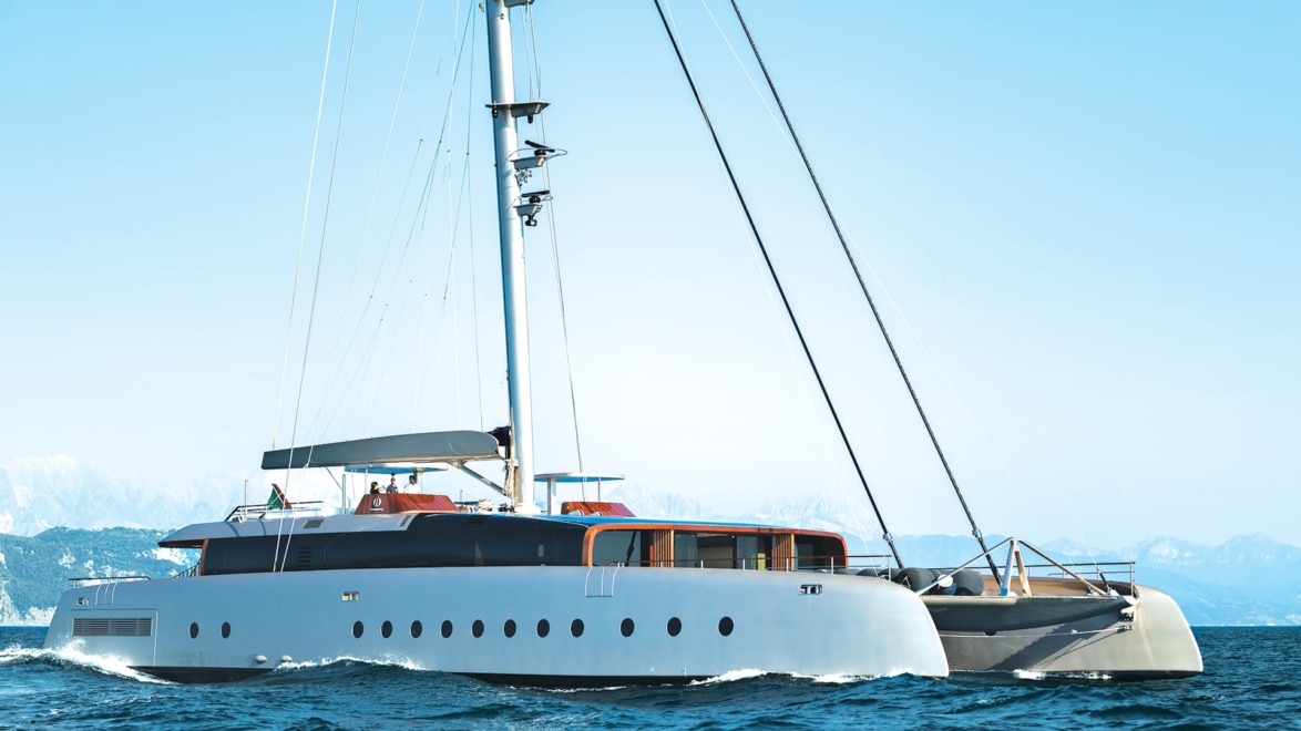 Large white sailing yacht navigating calm blue waters with mountains in the background.