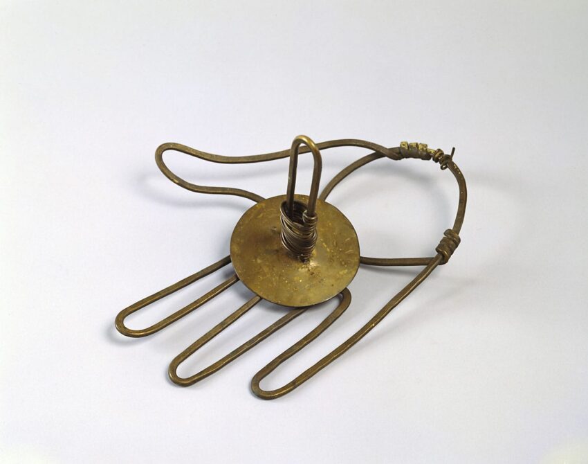Bronze hand-shaped hair ornament with looped fingers on a flat base and a metal loop in the center, used for ceremonial purposes.