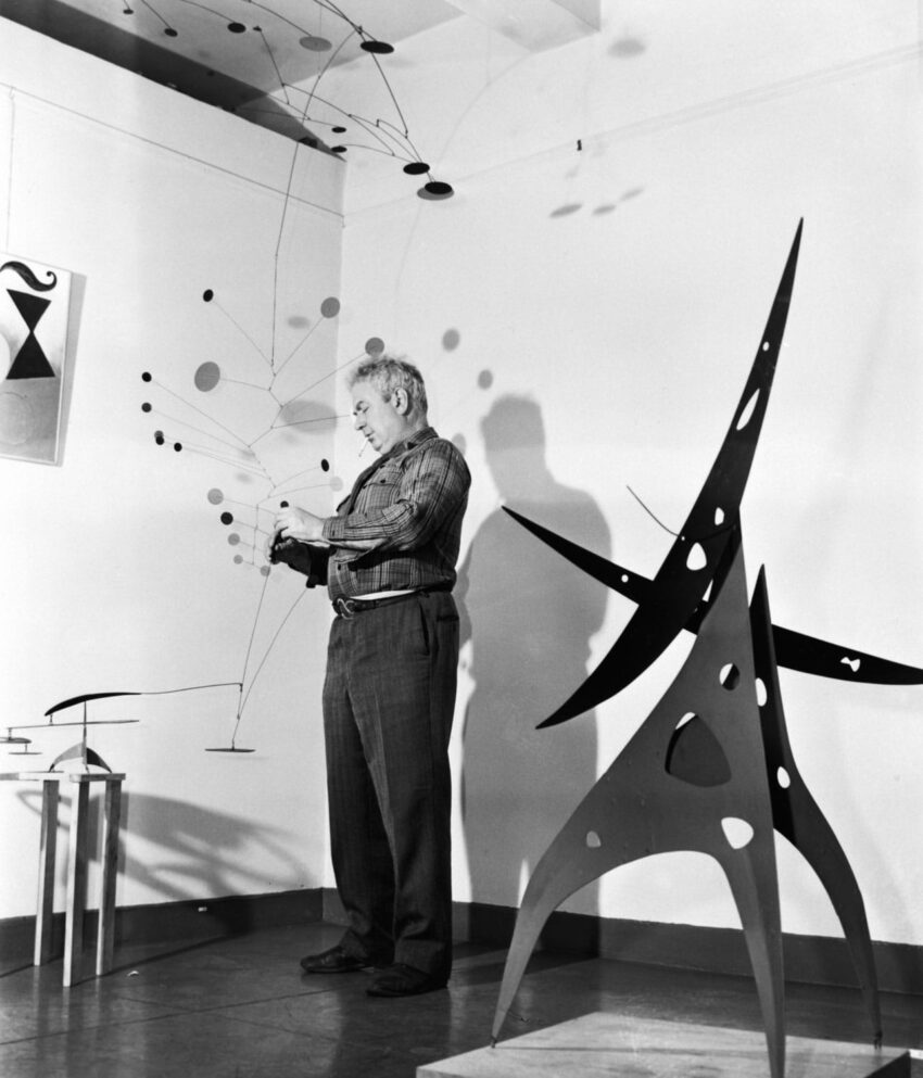 Artist working in a studio with abstract sculptures and mobiles displaying various geometric shapes and forms.