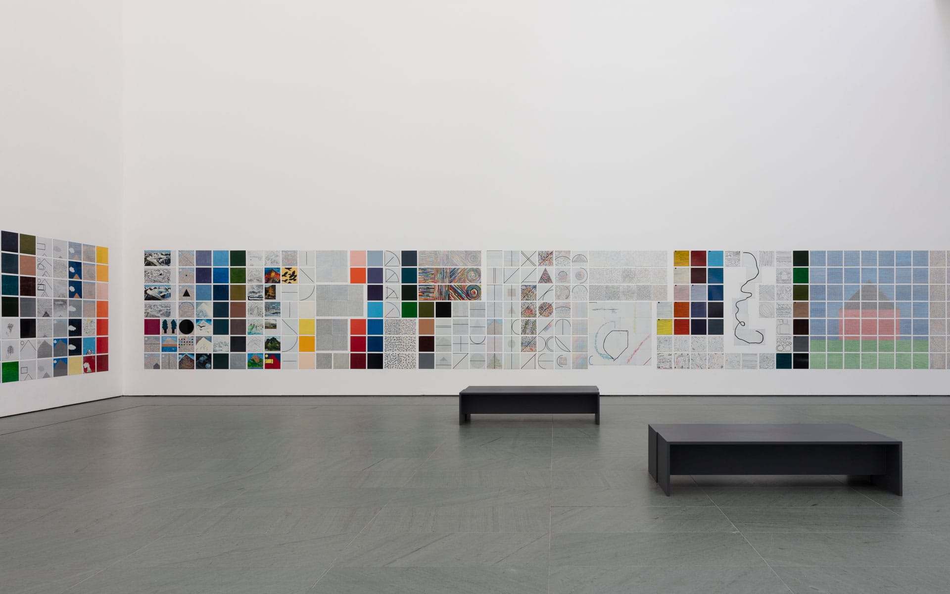Art gallery with colorful tiled wall display and two black benches on a gray floor.