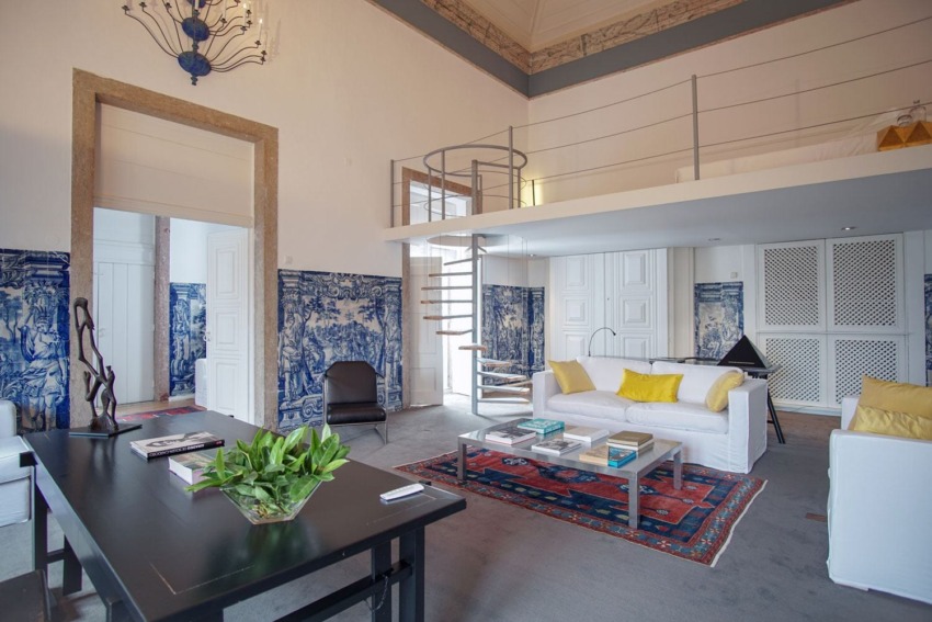 Spacious modern living room with white sofas, decorative tiles, a black table, and a spiral staircase leading to a loft.
