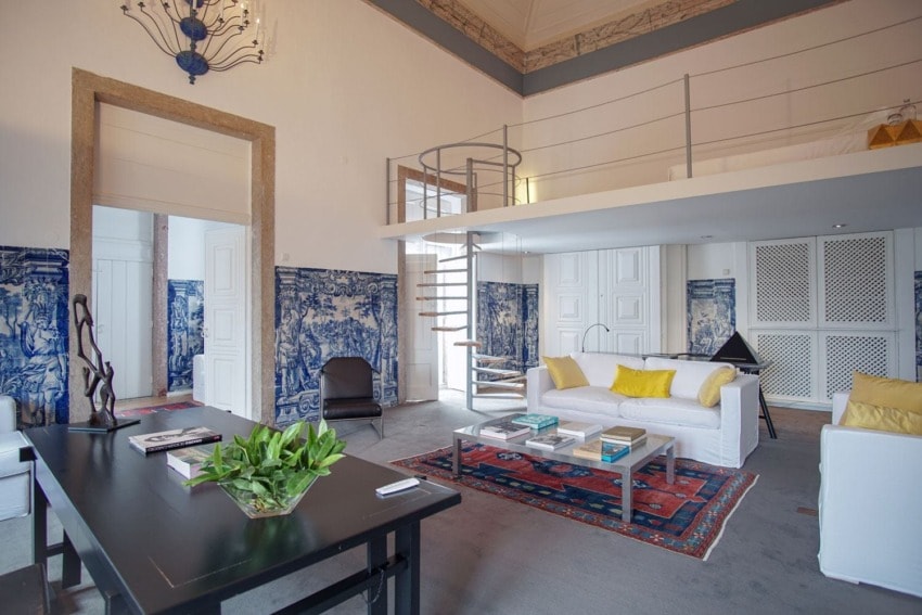 Spacious modern living room with white sofas, decorative tiles, a black table, and a spiral staircase leading to a loft.