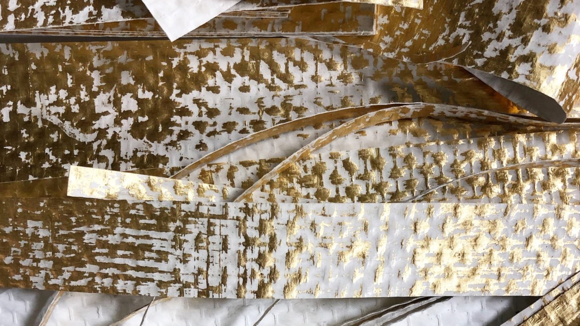 Abstract composition of overlapping white and gold textured paper strips.