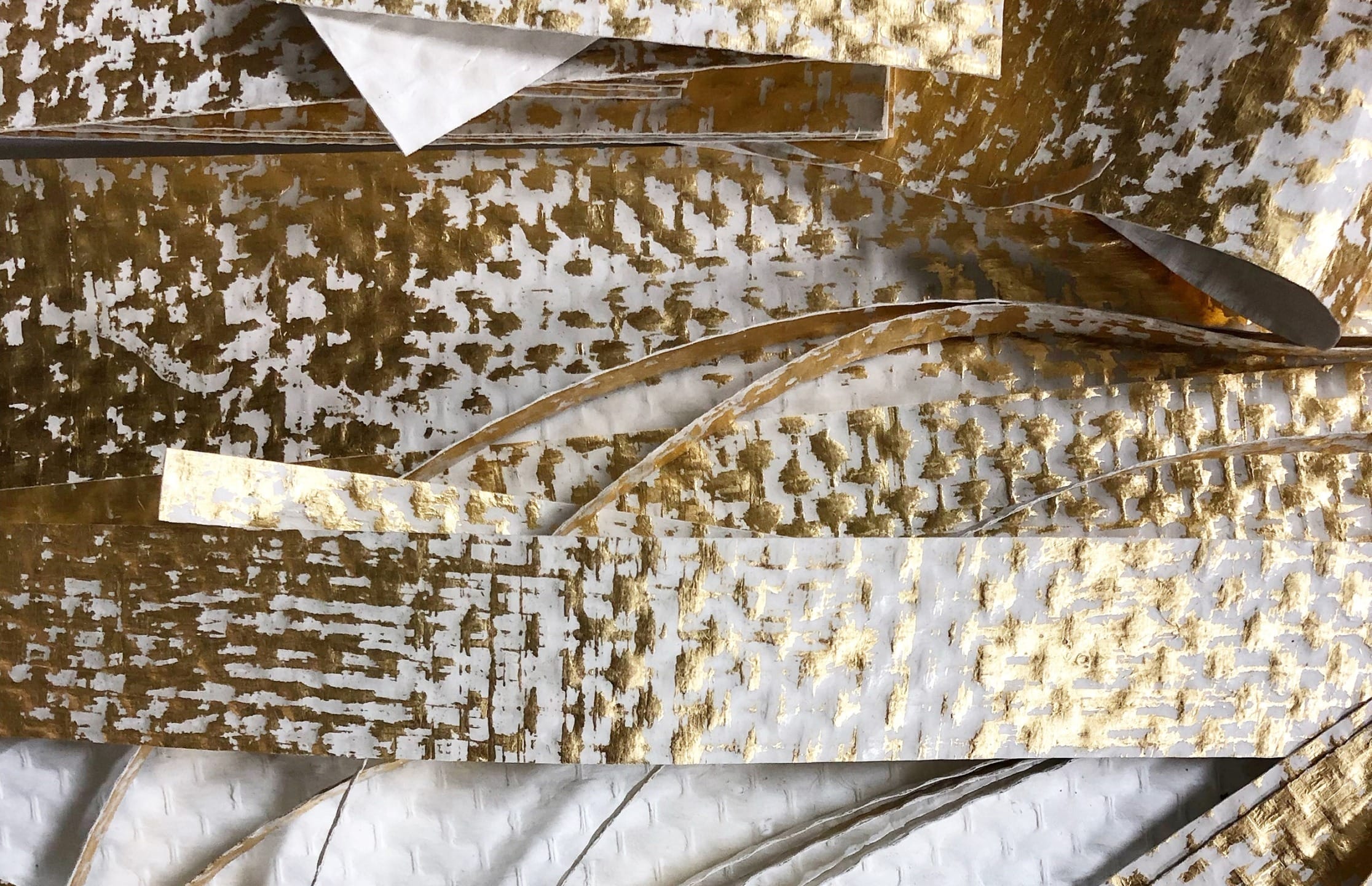 Abstract composition of overlapping white and gold textured paper strips.