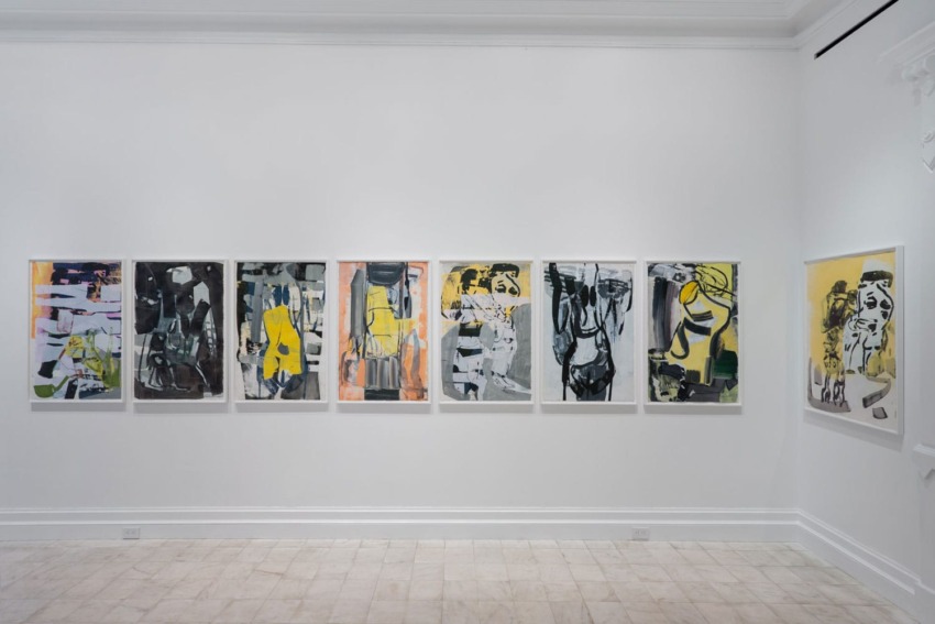 Art gallery room with a series of abstract paintings displayed on a white wall, featuring varied colors and forms.