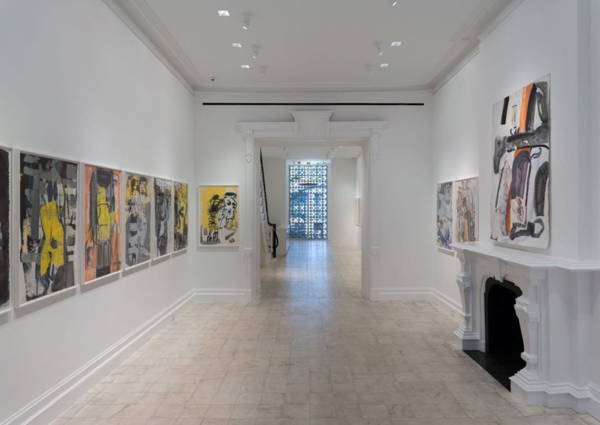 Art gallery hallway with paintings on white walls and a decorative fireplace.