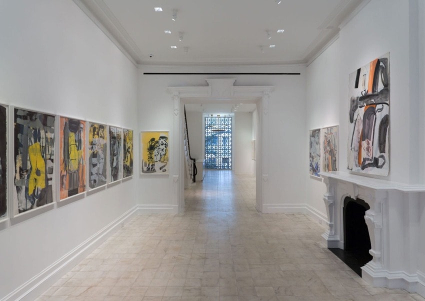 Art gallery hallway with paintings on white walls and a decorative fireplace.