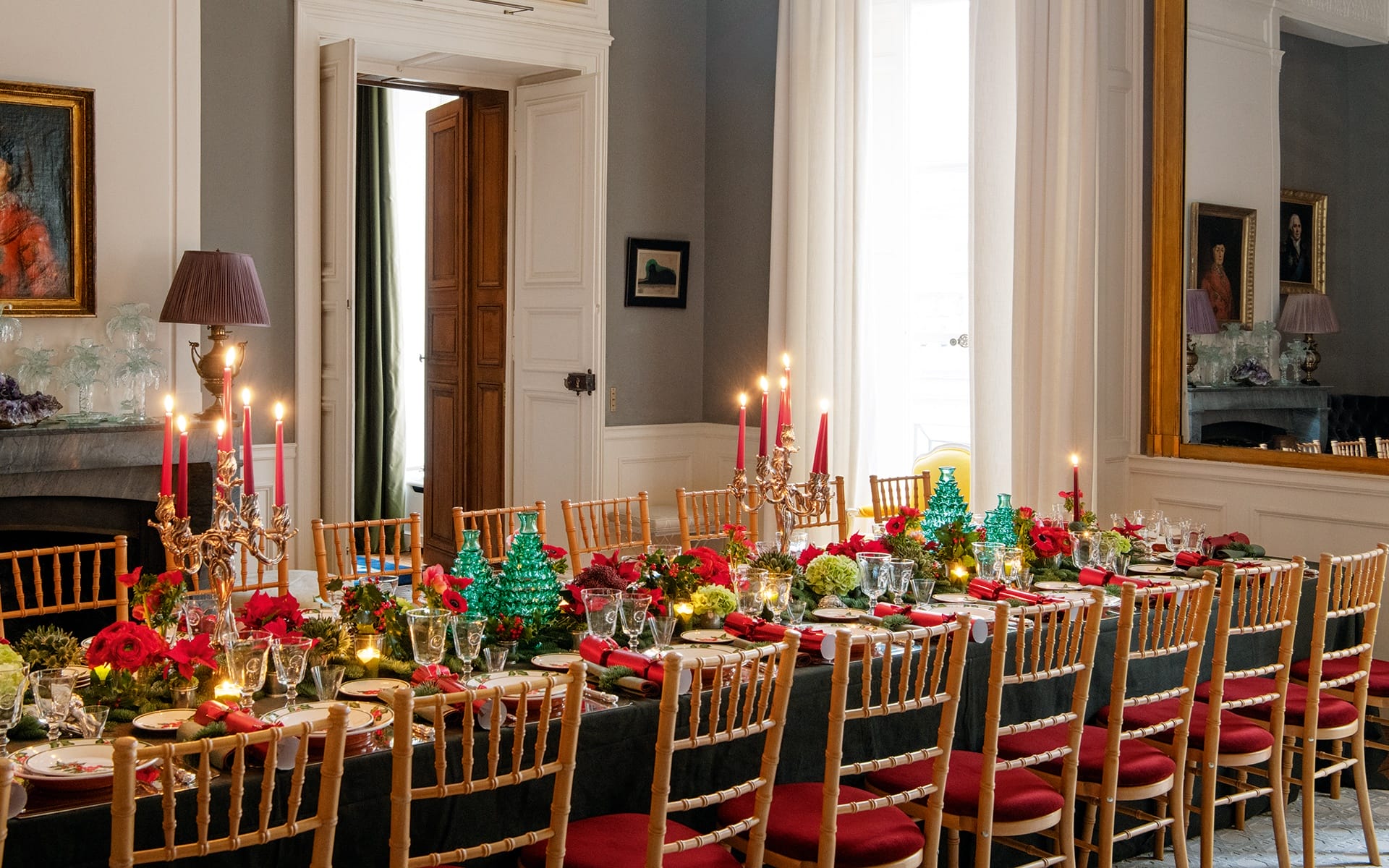 Elegant dining room with a long table set for Christmas dinner, featuring red and green decorations and candlelit ambiance.