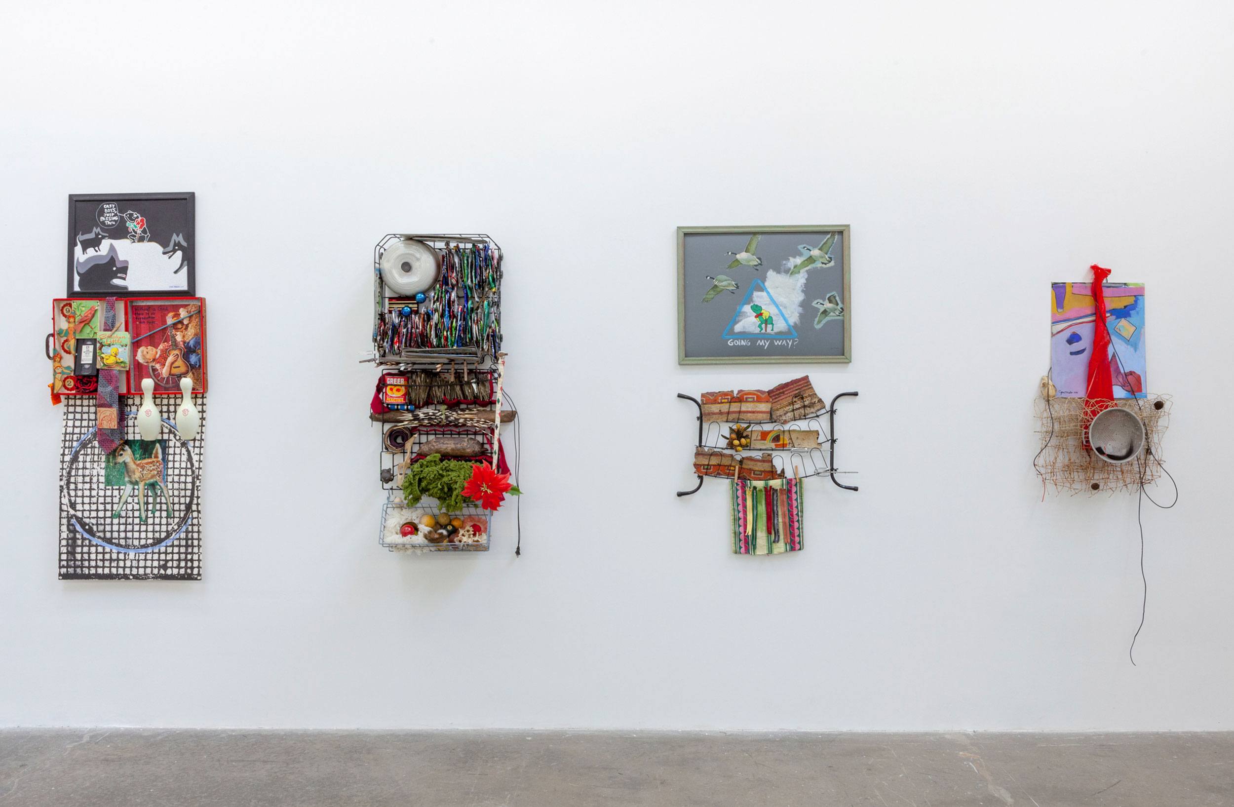 Four mixed media artworks featuring various colorful and eclectic objects mounted on a white gallery wall.