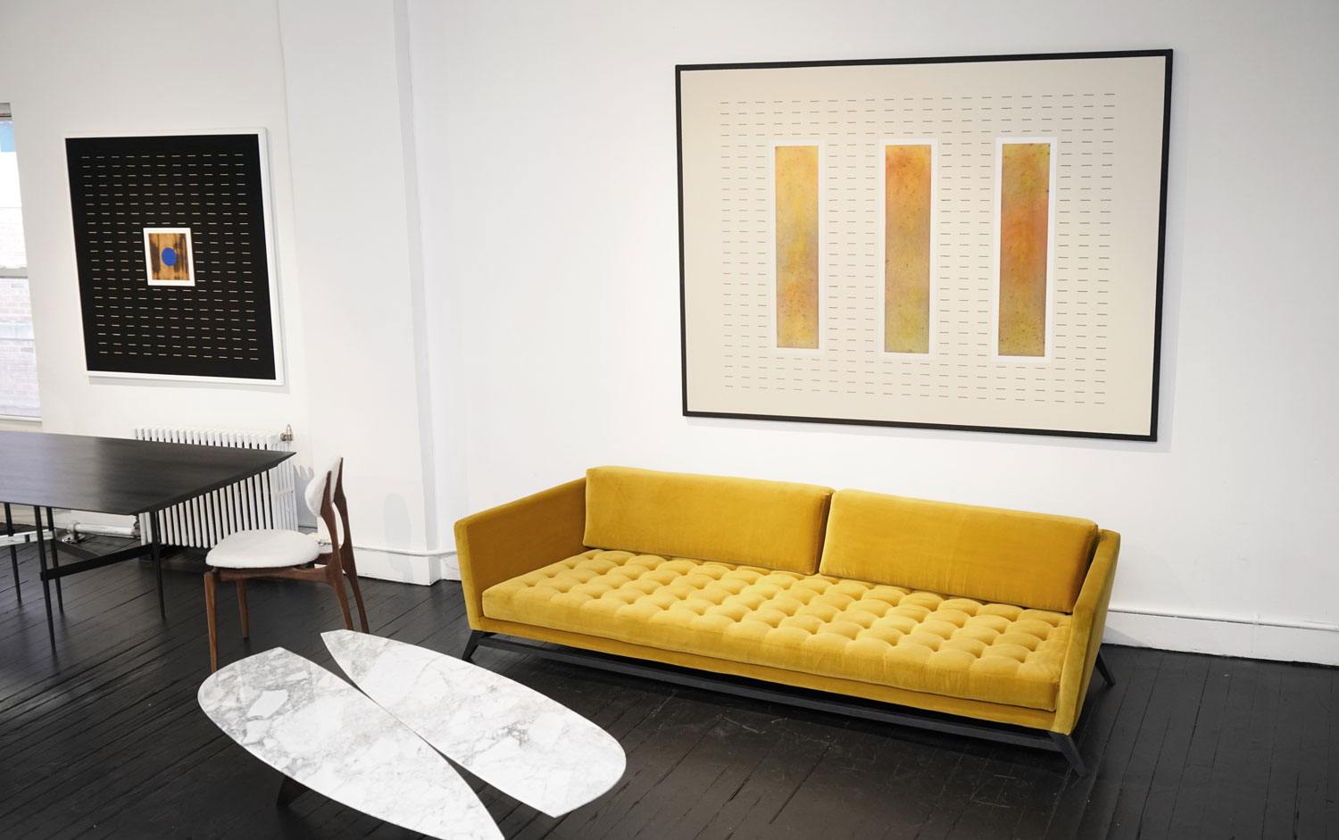 Modern living room with a mustard yellow sofa, abstract wall art, black table, white chair, and oval marble coffee table.
