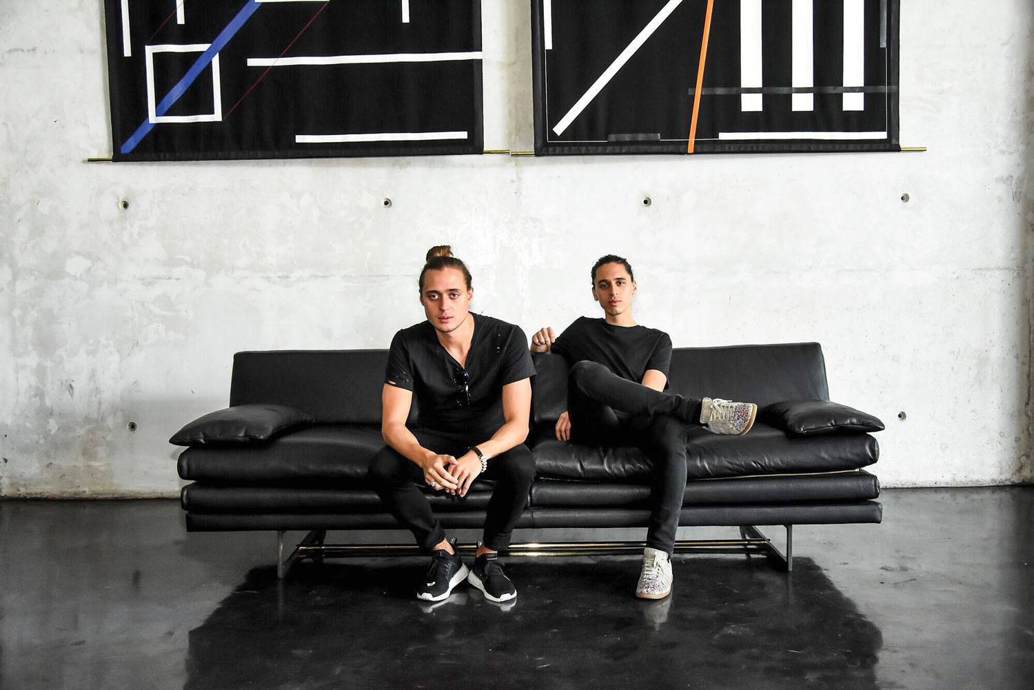 Two people sitting on a black sofa in a modern room with geometric wall art in the background.