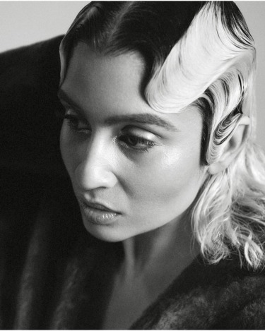 Monochrome portrait of a person with styled wavy hair and contemplative expression, looking away from the camera.