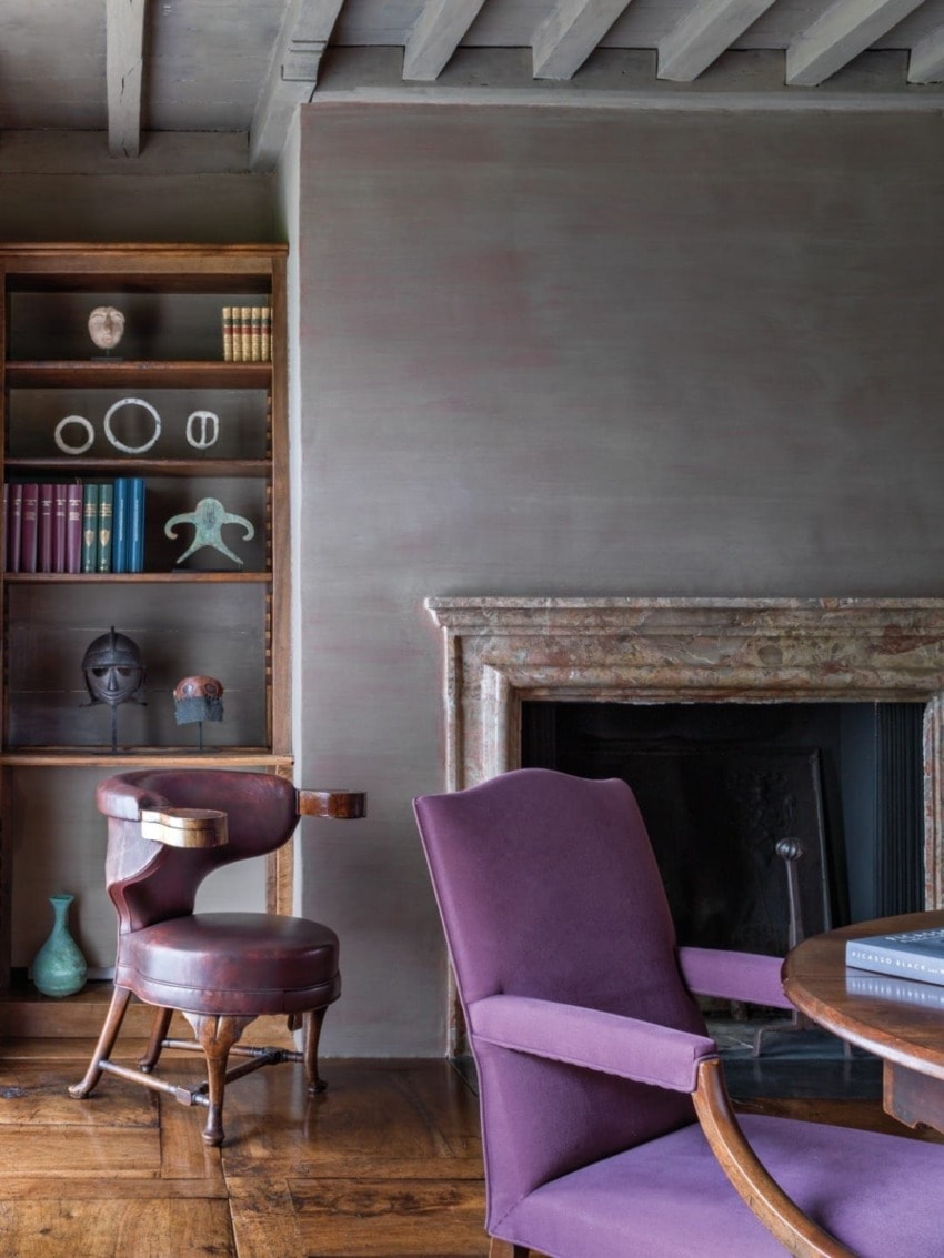 Vintage room with purple chairs, wooden floor, rustic bookshelves, and a stone fireplace, creating a cozy and elegant ambiance.