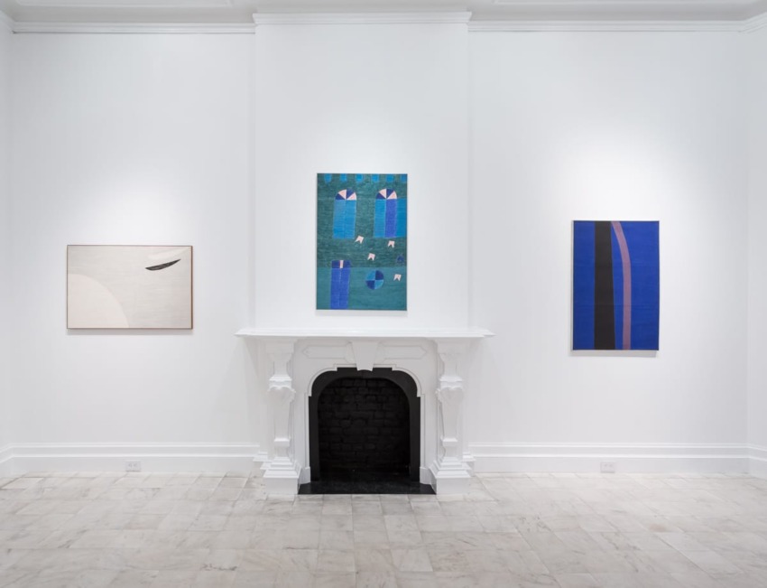 Art gallery wall with three abstract paintings and a decorative white fireplace in a spacious, minimalist setting.