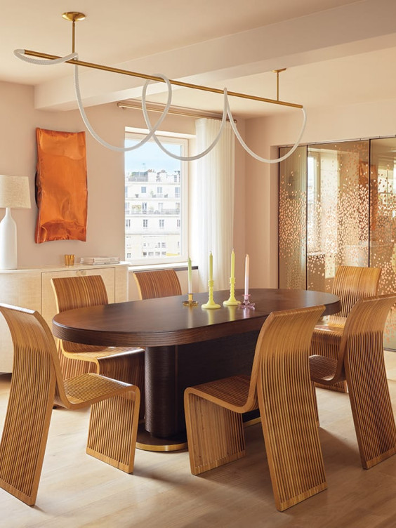 In the dining area, Pailleret installed a whimsical light fixture by Luke Lamp Co. above the client's vintage chairs and table, accented with Loewe candleholders. A flea market plaster lamp perches on a cabinet by Pailleret beneath a Thea Djordjadze metal wall sculpture, whose tones are echoed by copper-leaf sliding glass panels custom painted by Solène Eloy.