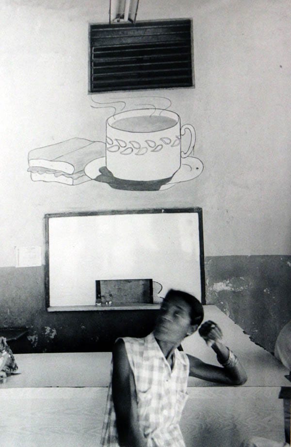 Person sitting in a room with a drawing of a sandwich and cup on the wall above.