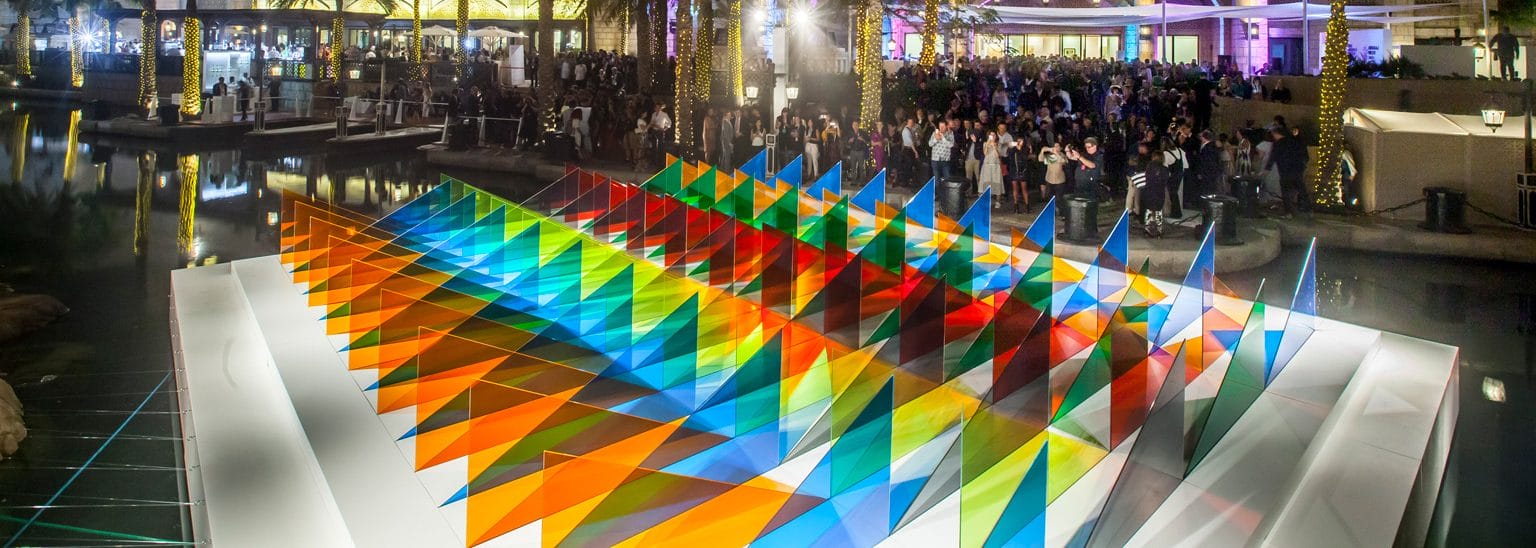 Colorful geometric art installation at outdoor event with crowd gathering in background during nighttime.