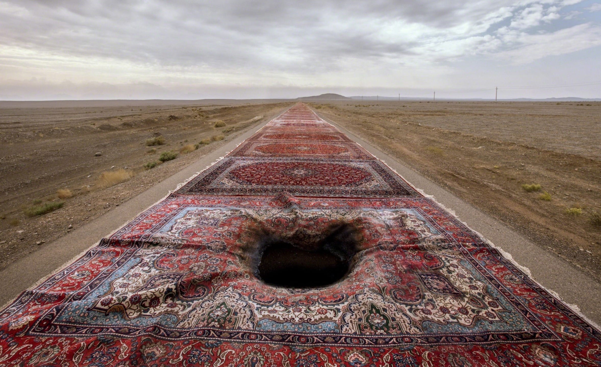Surreal scene of a road covered with Persian rugs leading to a distant horizon, featuring a hole in one carpet.